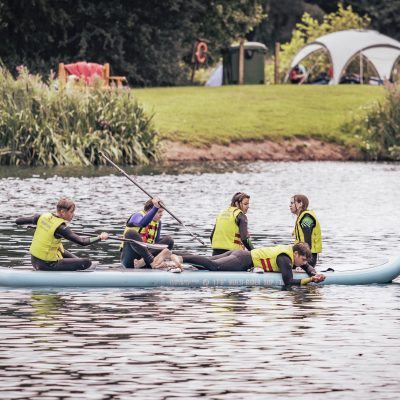 A group of people in yellow life jackets paddling a light blue inflatable kayak.