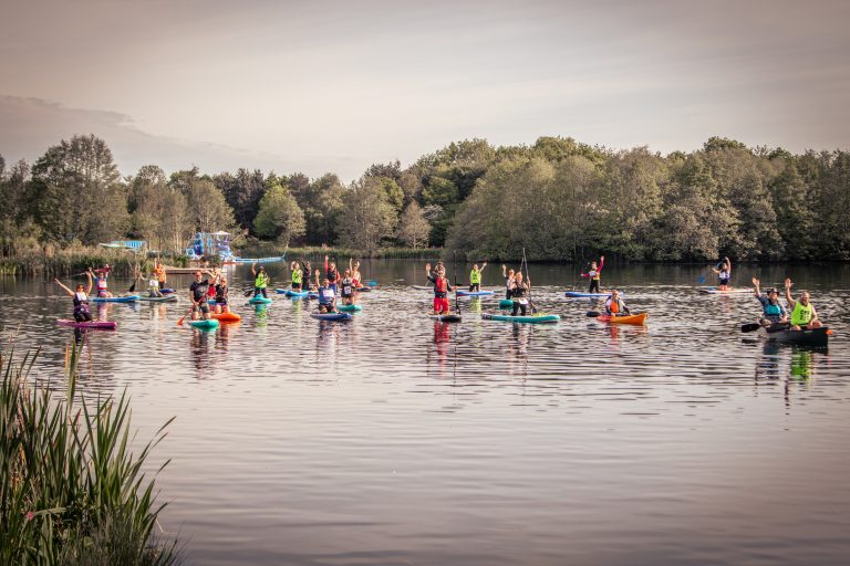 A group of people paddleboarding in colorful kayaks and canoes on a lake.
