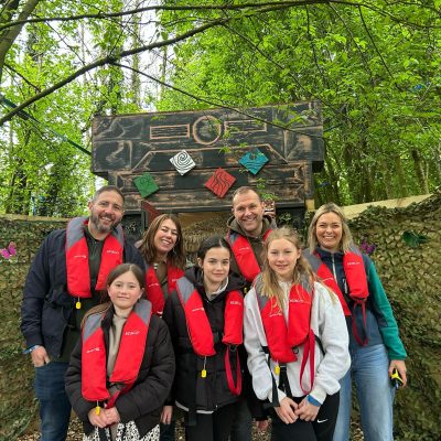 A group of people wearing life jackets pose in front of a wooden sign with various decorations.