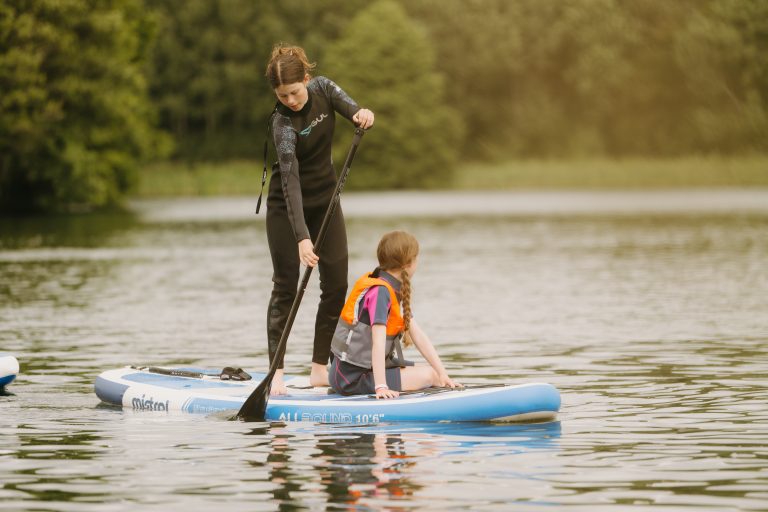 A woman and a child paddle on an inflatable stand-up paddleboard.