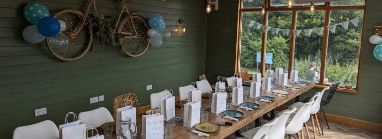 A long wooden table set with plates, glasses and bags of gifts for a celebration.
