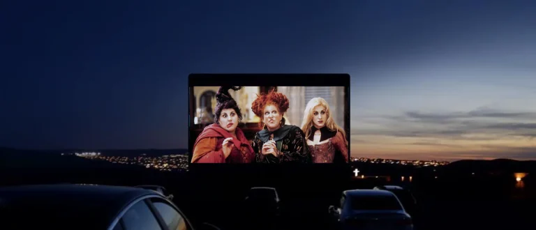 A group of people watching a movie on an outdoor screen during dusk.