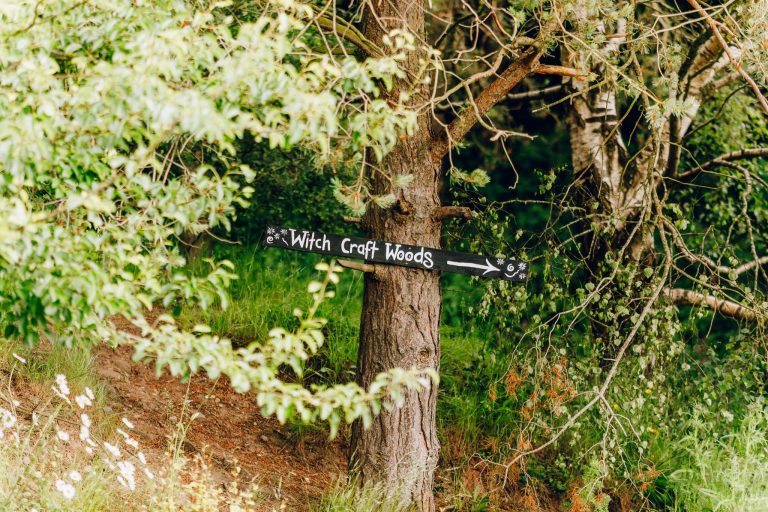 A signpost in a wooded area with the words 'Witch Craft Woods' and an arrow pointing right.