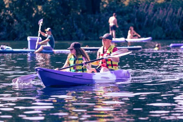 Two people wearing life jackets kayaking on calm water.