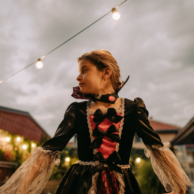 A woman dressed in a black and red Victorian costume with lace sleeves, standing outdoors at night.
