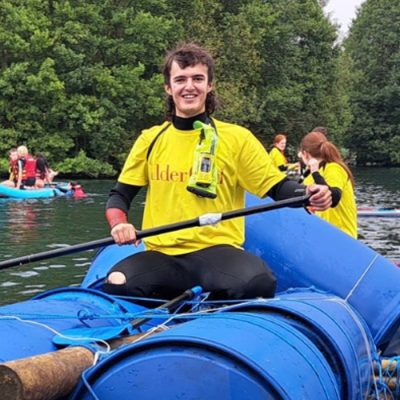 A person in yellow and black wetsuit paddling a blue kayak with others nearby.