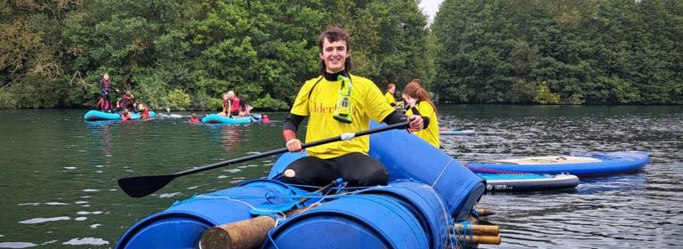 A person in yellow and black wetsuit paddling a blue kayak with others nearby.